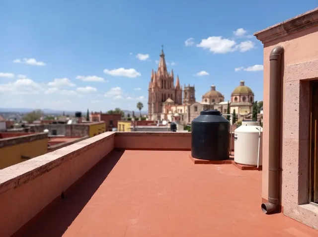 Azotea con tinaco negro, tanque blanco y bajante limpia, con la parroquia al fondo
